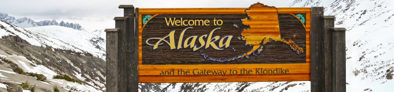 Welcome sign to alaska with mountains in the background